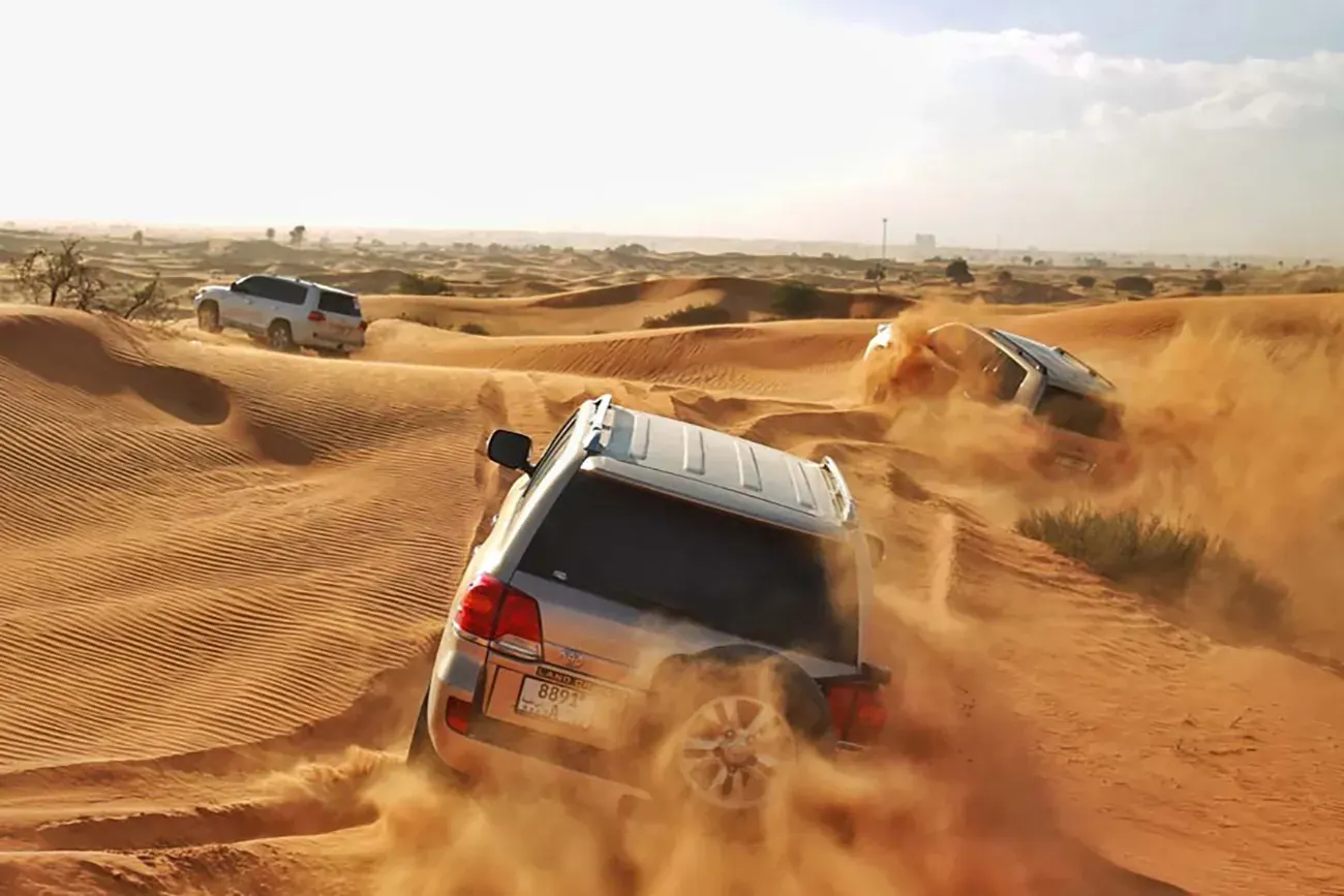 Safari vehicles travelling across the desert dunes