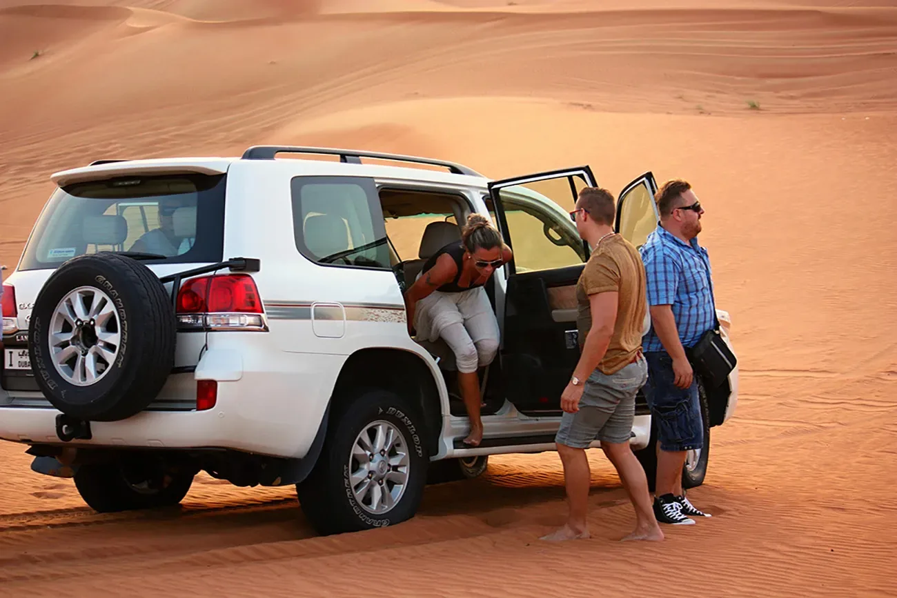 Guests beside their safari vehicle at a desert photo stop