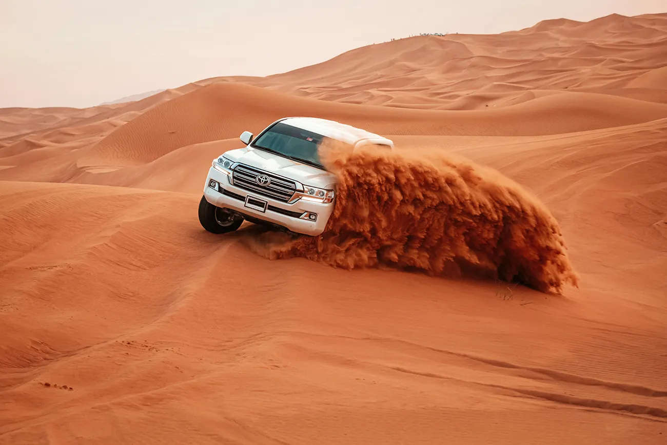 A desert safari vehicle turning across Dubai red dunes
